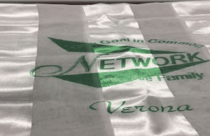 A white satin sash with green text that reads: "Goal in Common, eNetwork, the Family, Verona".
